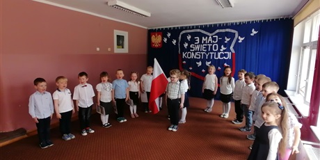 Powiększ grafikę: Dzieci w półkolu, na środku chłopiec, po lewej stronie flaga Polski